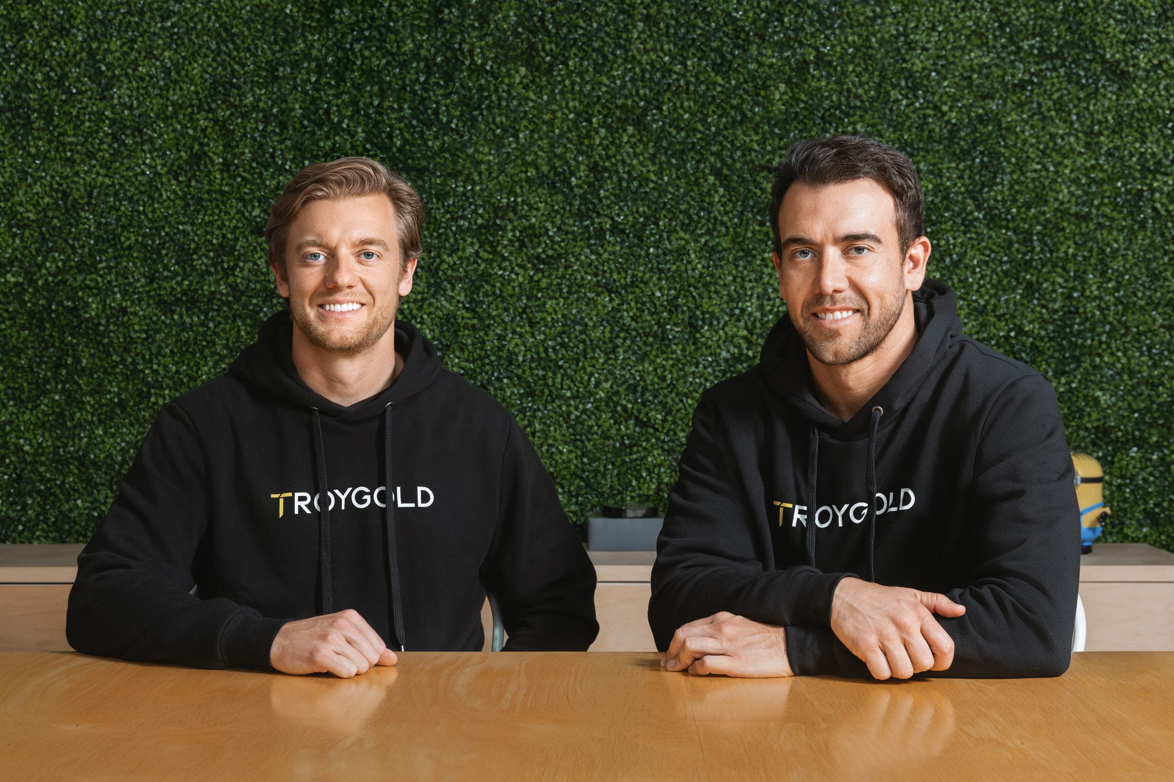 Troygold co-founders Dane and Bastiat Viljoen, seated side by side in Troygold hoodies.